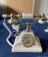 White porcelain telephone with handset resting on gold-tone cradle against blue cloth background