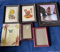 Top view of two fabric wall hangings and four assorted picture frames laid on blue fabric.