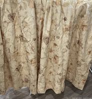 Close-up of curtains showing beige fabric with floral pattern in browns and muted oranges.