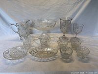 Full view of 10 American pressed glass items, including a large pitcher, footed compote, goblets, sauce dishes, creamers, celery vase, and olive dish. Clear glass with various pressed patterns.