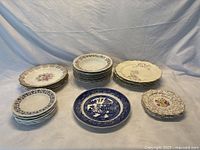 Overall lot view showing stacks of assorted porcelain plates and bowls in varied patterns including floral, blue and white, and classic black designs.
