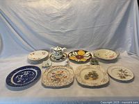 Wide view of assorted British porcelain plates and items arranged on table against blue backdrop showing variety of floral and patterned china.