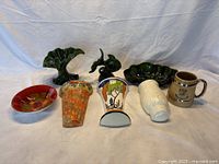 All the pottery and porcelain items arranged on a cloth background showing nine distinct items including bowls, vases, figurine, mug, and wall pockets