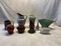 Wide shot of all nine pottery and porcelain items including various vases, pitchers, jugs, and pots displayed on a draped cloth.