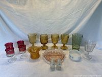 Full lot showing various colored glass goblets, tumblers, relish dish, salt & pepper shakers, and juice glasses arranged on a table.
