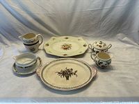Shows overall set including creamer, covered sugar bowl, serving platters, pitcher, and gravy boat with attached plate.