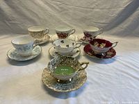 Six assorted Royal Stafford teacup and saucer sets arranged on white fabric background showing variety of patterns and colors.