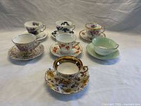 Full view of six assorted vintage teacup and saucer sets with varied floral patterns, colors, and gold trim