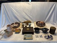 Wide image showing all items on display including coffee tin, ceramic tiles, collector plates, wood carving, bottles, and small decorative boxes