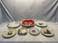 Seven assorted German porcelain plates on a white backdrop, including various designs such as figurines, flowers, and perforated edges.