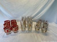 Photo showing all 18 glassware items arranged in groups - red and gold paisley cocktail glasses on left, frosted Pine Comb tumblers in middle, clear Pine Comb glasses on right.