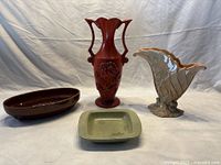 Four ceramic items: a reddish-brown handled floral vase, a large beige leaf-shaped vase, a brown oval serving dish, and a small square ashtray/soap dish.