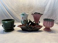 Wide view of five ceramic items showing variety of colors and shapes including green, pink, and floral pattern pieces.