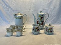 Noritake Komaru mocha pot set with 4 cups on left, Himark mocha pot set with creamer and sugar bowl on right against a blue cloth background