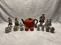 Front view of all porcelain items including 4 figurines, tomato ware teapot, condiment shakers and toothpick holders arranged in a line.
