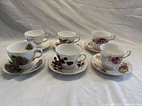 Six floral patterned vintage teacup and saucer sets displayed in two rows with different floral designs and gold edging.