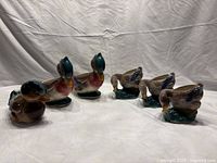 Six Royal Copley duck planters, two wood ducks and four mature ducks eating grass, arranged together on a neutral backdrop showing various angles.