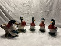 Five ceramic mallard duck planters and figurines arranged on a white cloth background showing the group in a frontal perspective.