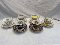 Six Royal Albert teacup and saucer sets arranged in two rows showing various floral patterns and gold rims.