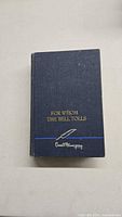 Front cover of the vintage book showing title and Ernest Hemingway's printed signature in gold on navy blue cloth.