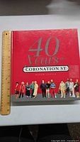 Front cover of the book showing the title '40 Years of Coronation St.' with cast images at bottom and ruler for scale.