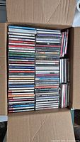 Top view of large box filled with about 54 assorted music CDs arranged neatly in rows