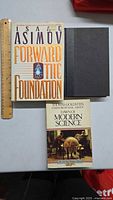 Photo showing 3 books from top view on a table with a ruler for scale: 'Forward the Foundation' by Isaac Asimov, 'Library of Modern Science' edited by Thomas Goldstein, and a dark hardcover book with no visible title.