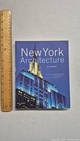 Front cover of the hardcover book 'New York Architecture: A History' showing the Empire State Building at night with blue tones.