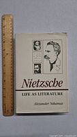 Front cover of the book titled 'Nietzsche Life as Literature' by Alexander Nehamas beside a wooden ruler for size reference.