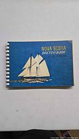 Front cover featuring a detailed sailing ship illustration and title 'Nova Scotia Sketch Book by L.B. Jenson' on blue background.