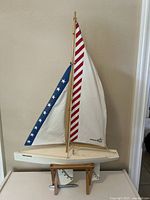 Full view of the model sailboat showing the wood hull and fabric sails in red, white, and blue with star pattern.
