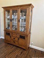 Front view of the wood display cabinet showing three lead glass upper doors revealing glass shelves and contents inside. Lower section has two wooden doors with lead glass inserts and four central drawers with metal pulls.