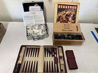 Image shows the Stratego game box with vintage cover and pieces, wooden box with black dominoes, and backgammon board with game pieces inside a brown case.