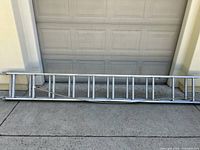 Full view of the 20 ft Cuprum aluminum extension ladder showing its length, metallic finish, structure, and some wear signs.