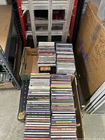 Boxes of CDs stacked on the floor of a storage or warehouse space, showing a large number of CDs in jewel cases.