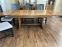 Full view of extended solid oak dining table with six chairs arranged around it, showcasing natural wood finish and two pull-out table extensions.