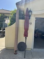 Photo of the rolled-up outdoor rug standing next to a closed red patio umbrella with base, against an outdoor wall.