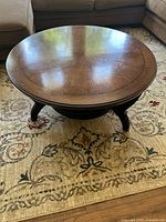 Front angled view showing round glossy wooden tabletop and curved legs.