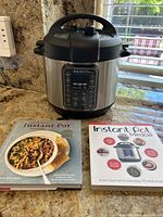 Instant Pot Duo Gourmet pressure cooker with two cookbooks on kitchen countertop.