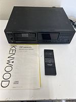 Front and top view of Kenwood DP-M6620 CD player, remote, and instruction manual on a white surface.