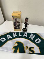 Photo showing MC Hammer bobblehead with its original box and Oakland A's flag laid flat.