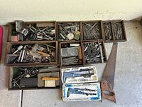 Overall collection of machinist tools arranged in wooden trays and cartons, including calipers, gears, a handsaw, files, gauge, and assorted metal tools.