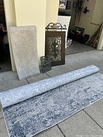 Photo showing the gray and blue ornate rug rolled out partly with decorative wall panels and upholstered bench leaning against a pillar.