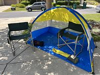 Wide shot showing the small yellow and blue camping tent with two green folding chairs inside and camping accessories on the floor