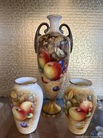 Photo of three Royal Worcester porcelain vases with fruit motif designs, showing front details and colors.