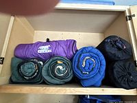 Top view of five rolled sleeping bags and two rolled sleeping mats inside a storage compartment.