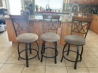 Set of three counter stools placed in a kitchen with tiled floor, showing metal frames, fabric seats, and wood backrests