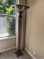 Full view of the floor lamp standing 6 feet tall near a window, showing the metal base and stained glass shade