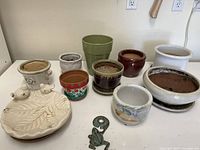 Overview of all ceramic and plastic planters along with tomato cage parts and a decorative frog figurine placed on a white table.