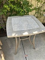 Square outdoor side table with mosaic tile top and curved metal legs in beige/brown tones